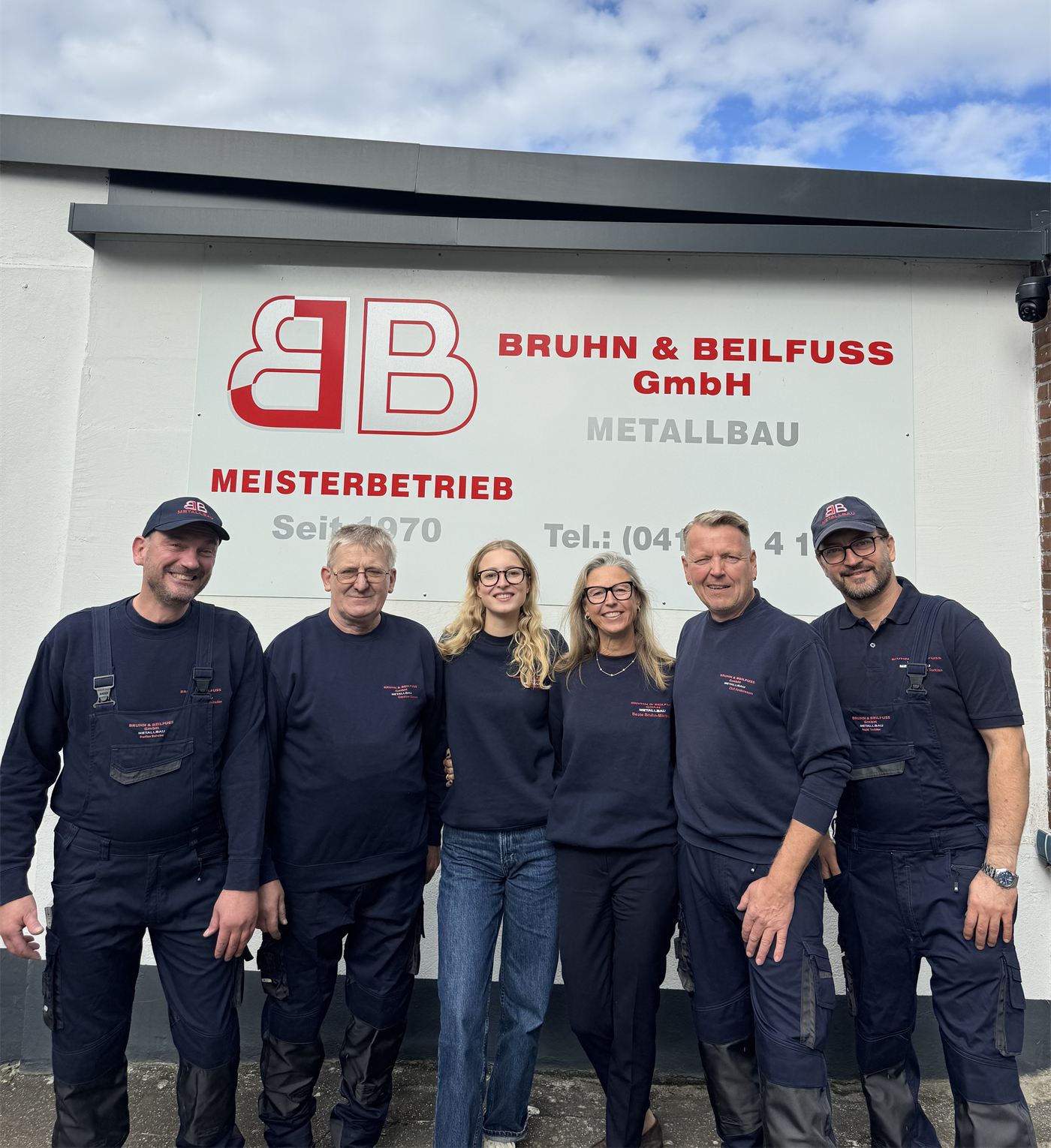 Das Team der Bruhn & Beilfuss GmbH in Arbeitskleidung vor dem Firmenschild am Sumpfweg in Halstenbek