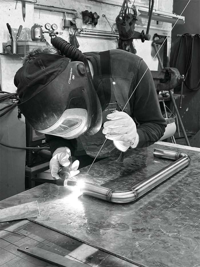 Schwarz-Weiß-Foto: Ein Metallbauer mit Schweißhelm beim WIG-Schweißen in der Werkstatt